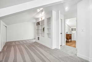 Carpeted room featuring a geometric pattern, built-in shelving, recessed lighting, and a closet with bifold doors