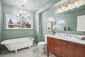 Bathroom featuring a white clawfoot bathtub with chrome fixtures, a wood-finish vanity with a white marble-patterned countertop and an integrated sink, a rectangular mirror with a gold-tone frame, and a gold-tone light fixture with fluted glass shades