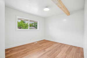 Bright interior space featuring wood-finish flooring, white baseboards, and a prominent wood beam accent