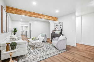 White-painted living space featuring a prominent wood-finish ceiling beam, recessed lighting, wood-finish flooring, and crisp white baseboards