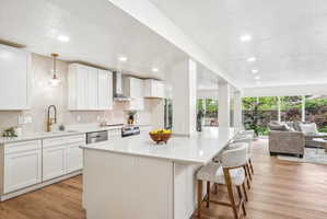 Contemporary kitchen featuring an extended island with seating, white shaker cabinetry, light-toned countertops, wood-finish flooring, and recessed lighting