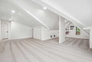 Spacious carpeted room featuring a sloped ceiling with exposed beams, recessed lighting, and a white interior door
