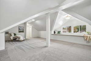 Expansive carpeted room featuring sloped ceilings, white painted walls, and white trim