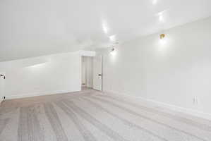 Spacious room with sloped ceilings, light-toned carpet, white walls, recessed ceiling lights, and two wall sconces