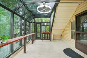 Glass-enclosed sunroom featuring a concrete floor, sloped glass ceiling, and a ceiling fan with integrated lighting