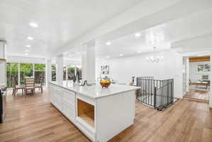 Expansive kitchen island with a light-toned countertop, wood-finish flooring, recessed lighting, white cabinetry, and a black metal spindle staircase