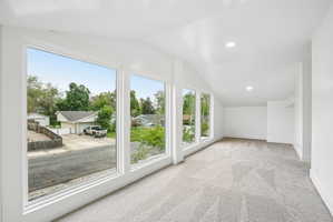 Spacious room featuring multiple large windows, vaulted ceilings with recessed lighting, and light-toned patterned carpeting