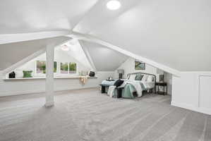 Spacious attic room with light gray carpeting and sloped white ceilings