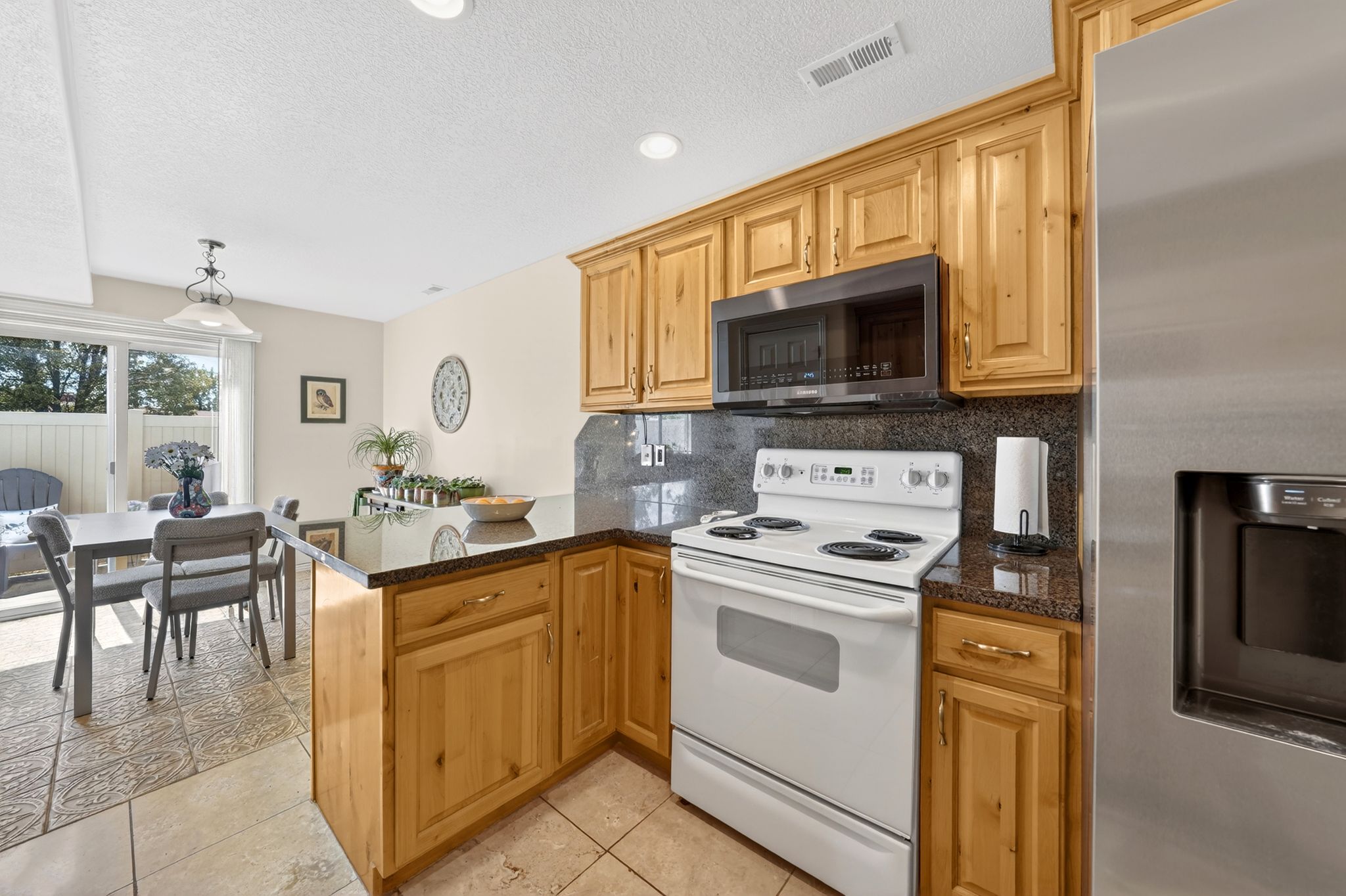 Kitchen featuring stainless steel appliances, a peninsula, light tile patterned floors, backsplash, and dark stone countertops