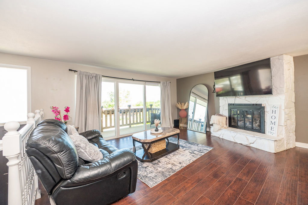 Living area featuring wood-finish flooring, a stone-clad fireplace with a hearth, and sliding glass doors opening to a balcony with a wood railing