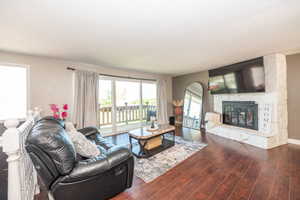 Living area featuring wood-finish flooring, a stone-clad fireplace with a hearth, and sliding glass doors opening to a balcony with a wood railing