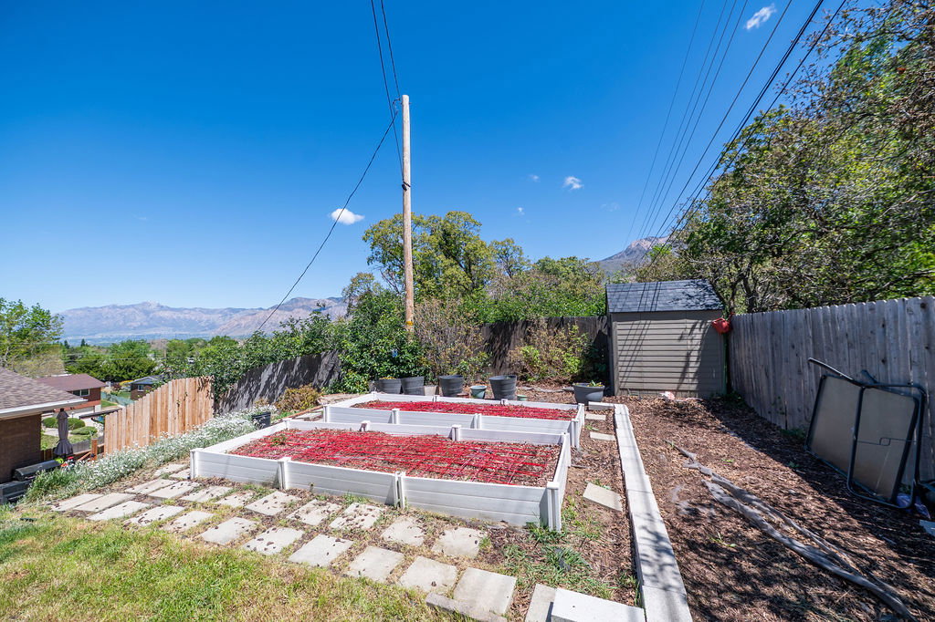 Terraced backyard featuring two raised garden beds with red ground cover, a natural wood privacy fence, and a storage shed with an asphalt shingle roof