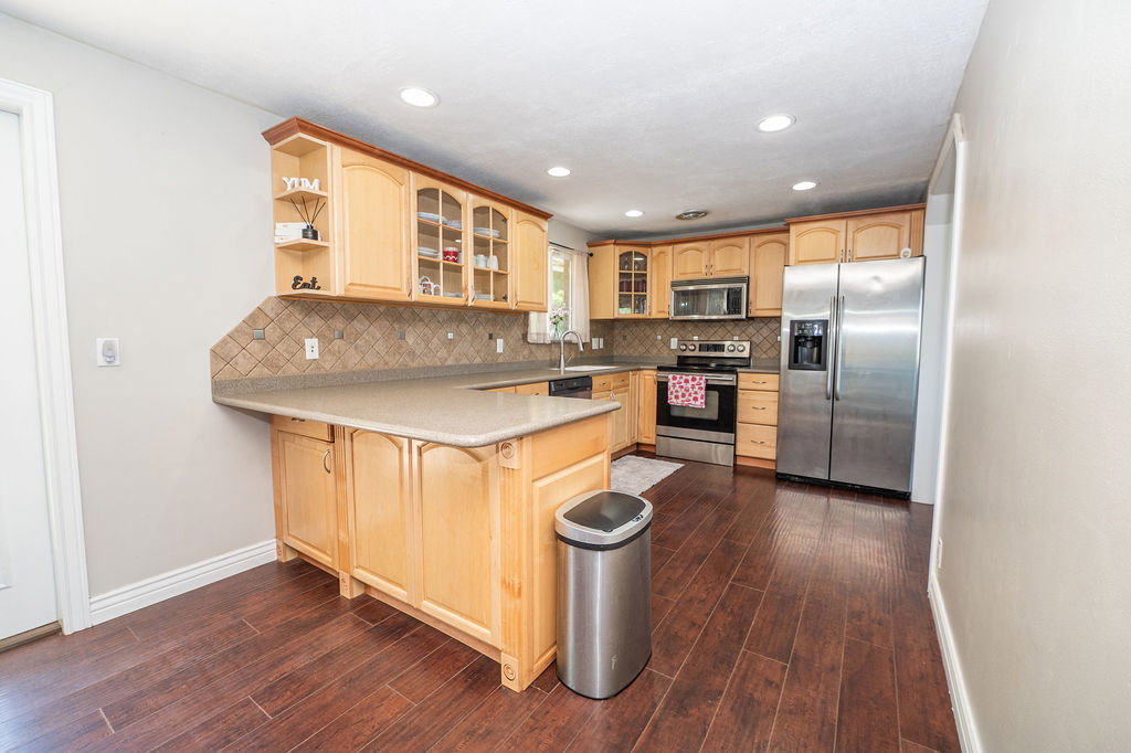 Kitchen featuring light wood cabinetry, stainless steel appliances, a tiled backsplash, wood-finish flooring, and recessed lighting