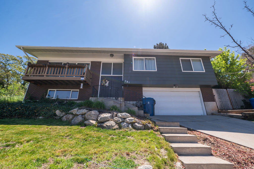 Split-level residence featuring a two-car garage, brick and siding exterior, front balcony, and concrete steps leading to the entrance