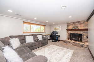 Spacious living area featuring a stone fireplace with a wood mantel, recessed lighting, carpet flooring, and a window with horizontal blinds