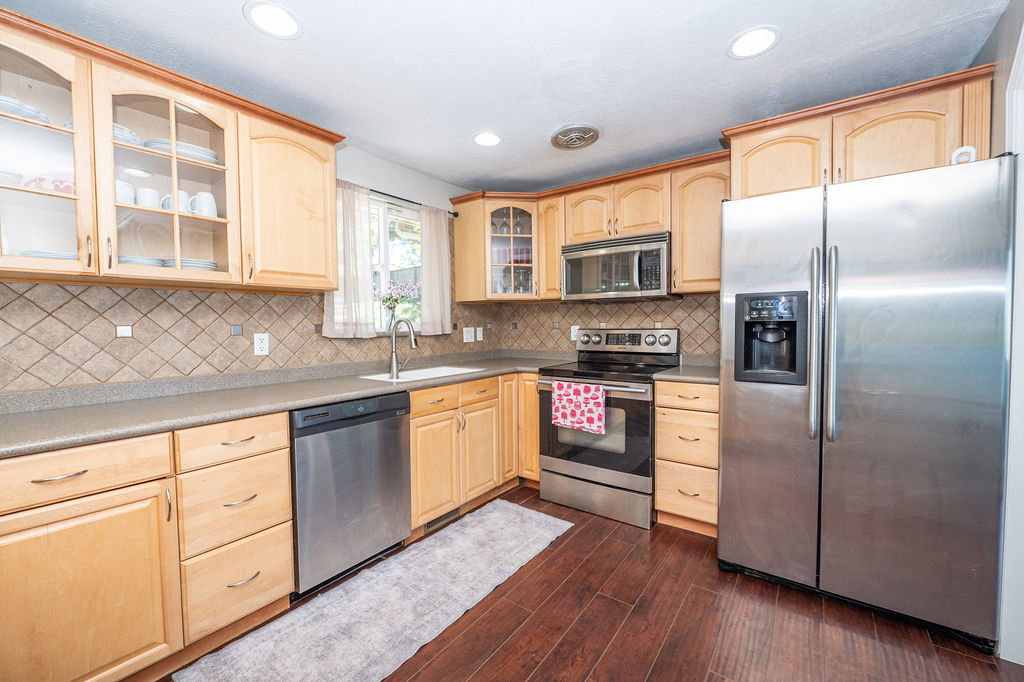 Kitchen featuring wood-finish cabinetry, stainless steel appliances, a tile backsplash, and composite countertops