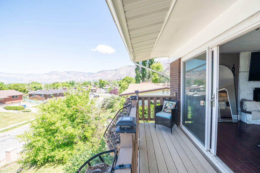 Exterior balcony featuring composite decking, wooden railing with post caps, and a white aluminum sliding glass door