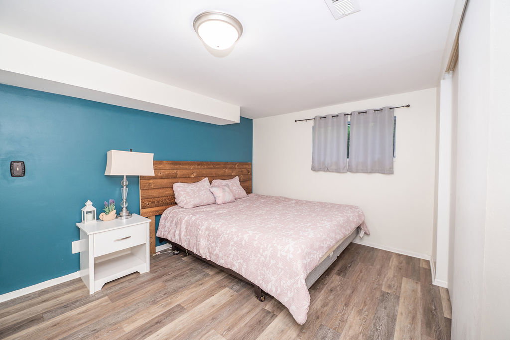 Bedroom featuring a striking teal accent wall, wood-finish flooring, and a flush mount ceiling light fixture