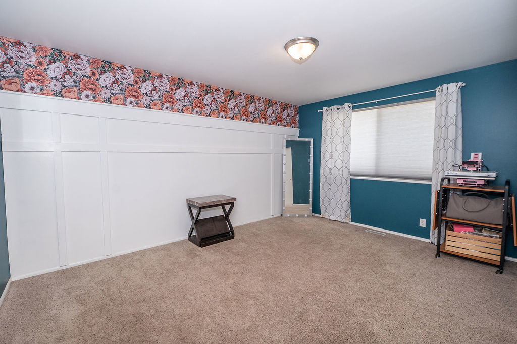 Spacious interior room featuring carpet flooring, board and batten wall detailing, floral pattern wallpaper accent, a large window, and a flush mount ceiling light fixture