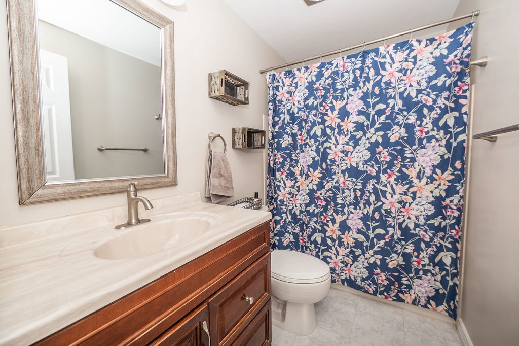 Bathroom featuring a wood-finish vanity with an integrated sink and brushed nickel faucet, a framed mirror, and light-toned tile flooring