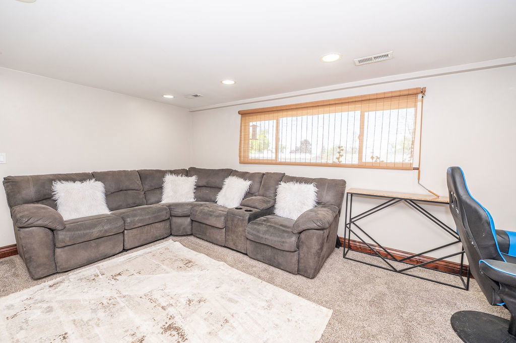 Recessed ceiling lighting illuminates a carpeted interior space with a window featuring wood-look blinds