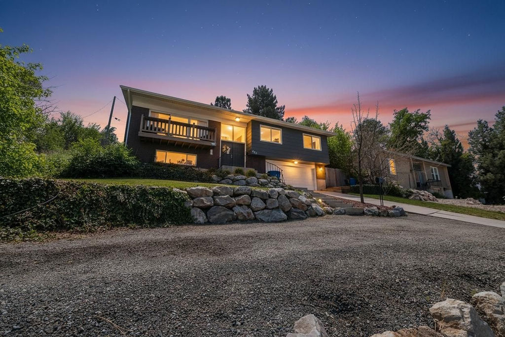 Contemporary split-level residence featuring a dark facade, contrasting white garage door, and an upper-level balcony with wood railing