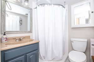 Bathroom featuring a vanity with a countertop sink, a white shower curtain, a toilet, a framed mirror, and a wall-mounted medicine cabinet
