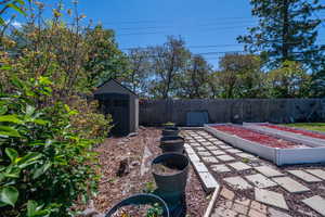Expansive backyard featuring a stepping stone pathway, multiple raised garden beds, a storage shed, and mature perimeter trees