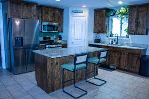 Kitchen featuring a central island with a light-toned countertop, wood-finish cabinetry, a stainless steel refrigerator, a matching stainless steel microwave, and a gas range