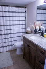 Bathroom featuring a wood-finish vanity with an integrated sink and granite-patterned countertop, ceramic tile flooring, and a white toilet