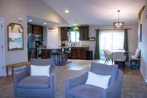 Open-concept living area featuring vaulted ceilings, wood-finish cabinetry, stainless steel appliances, and a sliding glass door leading to an outdoor space