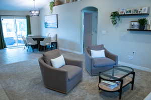 Open concept living area featuring textured carpeting, a tiled dining area with a contemporary chandelier, and sliding glass doors