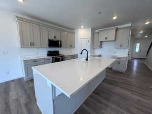 Spacious kitchen featuring a large central island with a white solid surface countertop, light gray cabinetry with black hardware, wood-finish flooring, a stainless steel microwave, and a black range