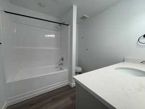 Bathroom featuring a white integrated tub and shower combination with chrome fixtures, a black shower curtain rod, a single vanity with a light-toned countertop, and wood-finish flooring