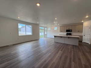 Open-concept living space featuring wood-finish flooring, recessed lighting, a kitchen island with a built-in sink, light-toned cabinetry, and sliding glass doors to the exterior