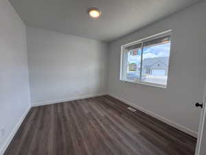 Spacious room featuring wood-finish flooring, crisp white walls, and a large window