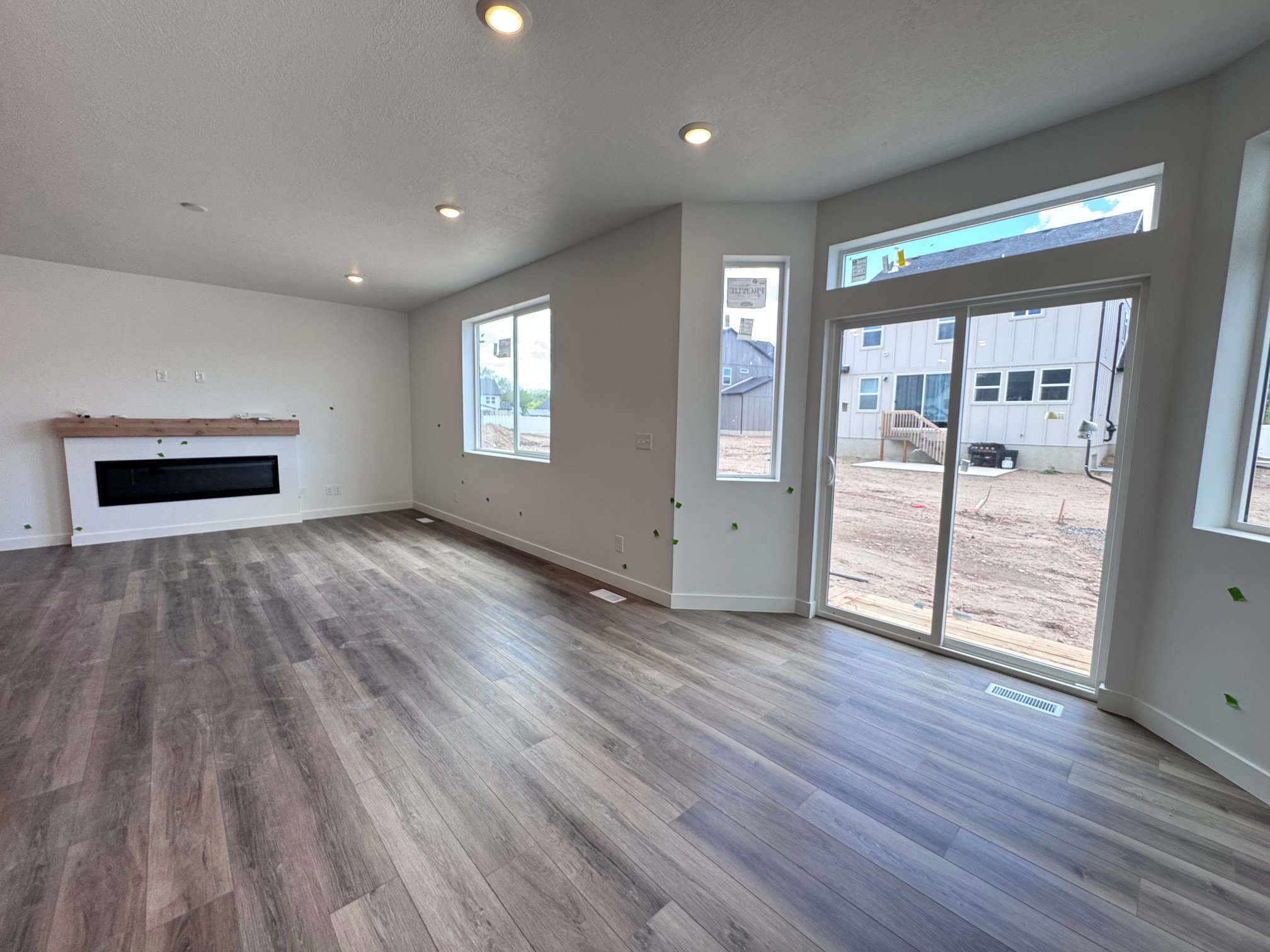 Spacious room featuring wood-finish flooring, a contemporary linear fireplace with a wood mantel, ample natural light from multiple windows, and recessed lighting