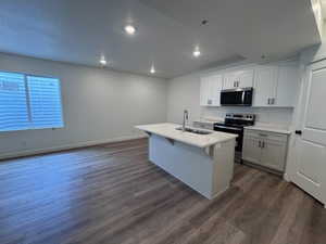 Open-concept kitchen featuring an island with an undermount sink, light-toned cabinetry, stainless steel appliances, and a window with blinds