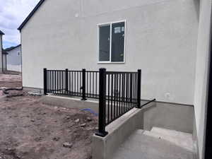 Basement access featuring a concrete staircase, black metal railing, and white stucco exterior