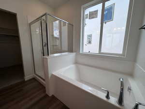 Soaking tub with chrome fixtures, glass-enclosed shower, wood-finish flooring, and a large window