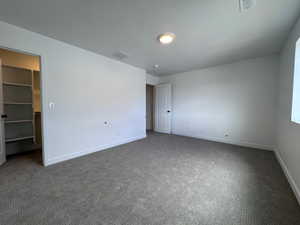 Spacious room featuring neutral carpet flooring, white painted walls, a built-in closet with shelving, a white paneled door, and a flush-mount ceiling light fixture