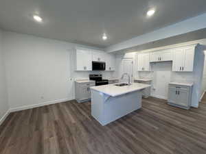 Kitchen featuring wood-finish flooring, recessed lighting, a central island with an integrated sink and gooseneck faucet, light grey base cabinetry, and white upper cabinetry with dark hardware