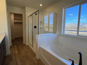 Bathroom featuring a built-in soaking tub with black fixtures, a glass-enclosed shower with black hardware, and wood-finish flooring