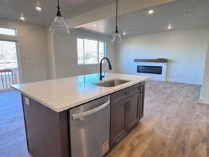 Kitchen island featuring a stainless steel undermount sink, gooseneck faucet, integrated dishwasher, and pendant lighting