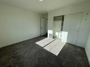 Spacious room featuring neutral carpeting, white painted walls, white trim, and a built-in closet with sliding panel doors