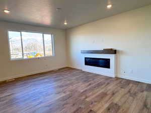Spacious room featuring wood-finish flooring, a contemporary linear electric fireplace with a dark wood-finish mantel, recessed ceiling lighting, and a large window