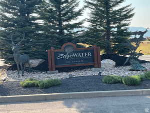 Custom wooden community signage with bronze deer and bird sculptures, surrounded by mature evergreen trees, decorative rock landscaping, and low-lying shrubs