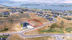 Elevated property lot outlined in red, featuring natural terrain and a backdrop of a large body of water