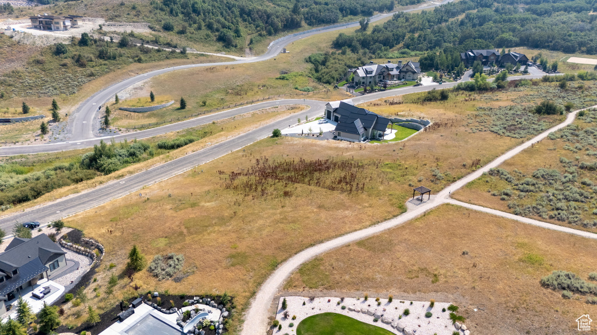 Expansive undeveloped land featuring natural terrain with scattered brush, a partially visible gravel path, and distant paved roadways