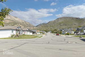 Residential street with a mountain backdrop, featuring single-story homes with attached garages, pitched roofs, and manicured lawns